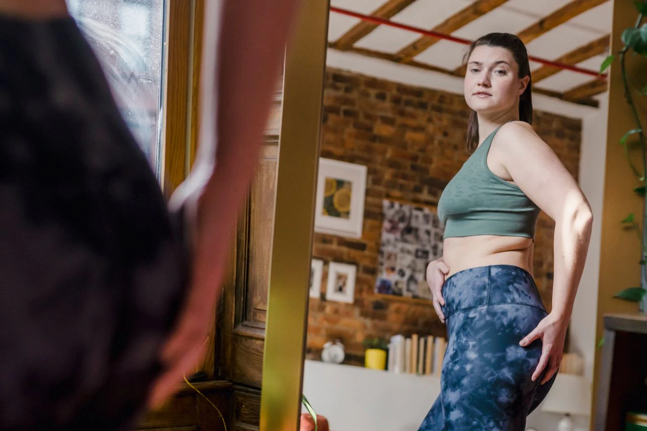 Woman considering post weight loss surgery after significant weight loss while looking in a mirror at home.